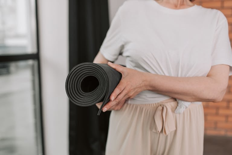 Close-up of a senior woman holding a yoga mat, ready for a session in a modern studio.