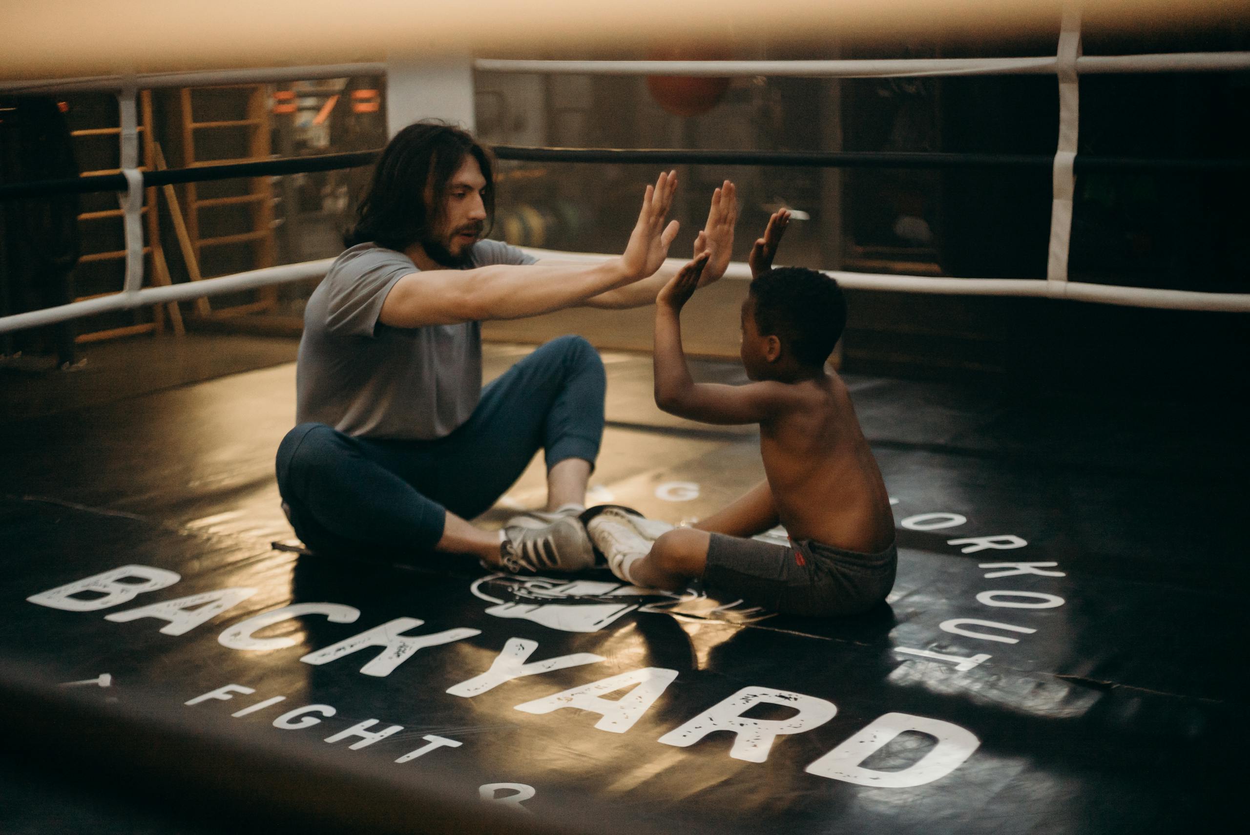 A coach and young boxer share a high-five during training in an indoor boxing gym.