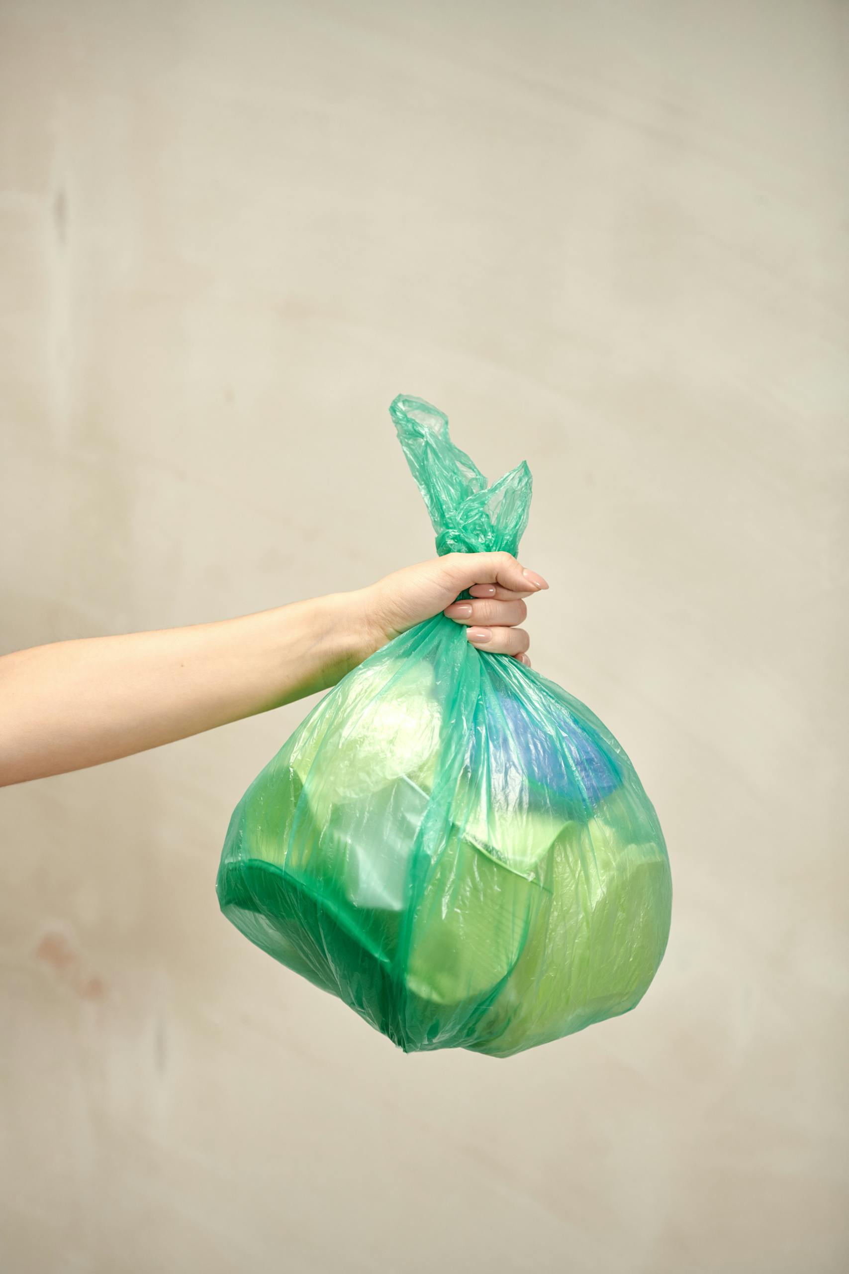A person holds a green plastic bag filled with disposal items representing waste management.