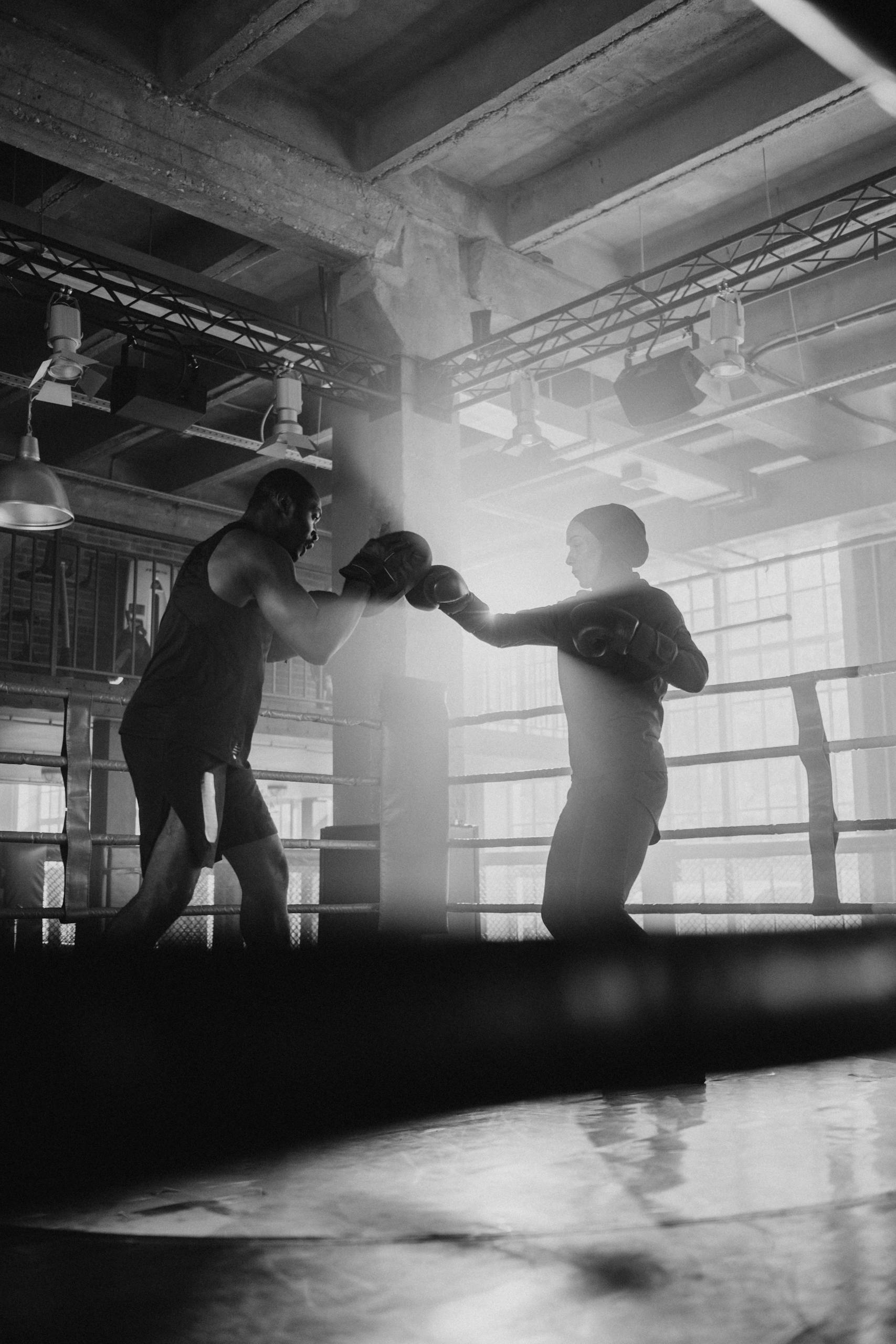 Intense sparring session between two boxers in a monochrome gym setting.