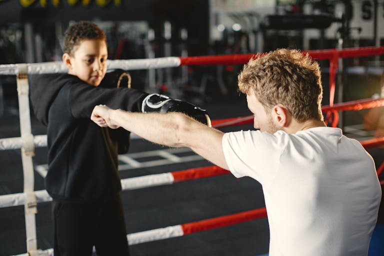 A young boy practices boxing techniques with a trainer in a gym. Mentorship in sports.