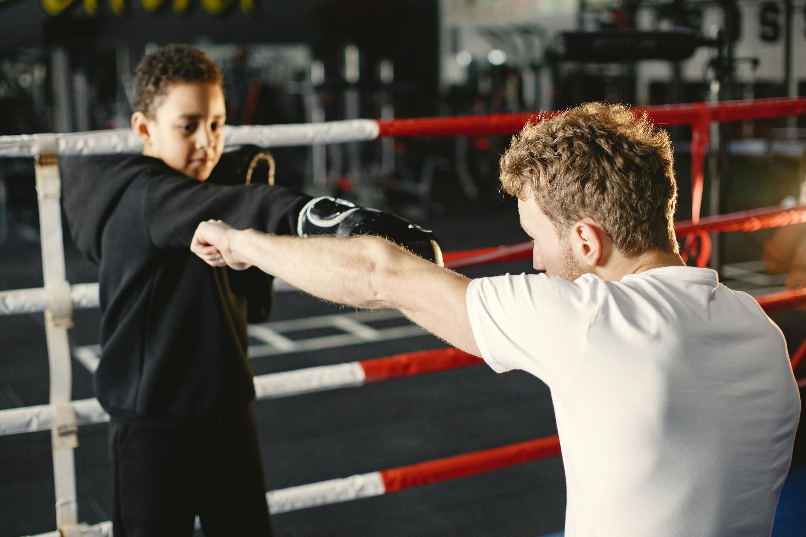 A young boy practices boxing techniques with a trainer in a gym. Mentorship in sports.