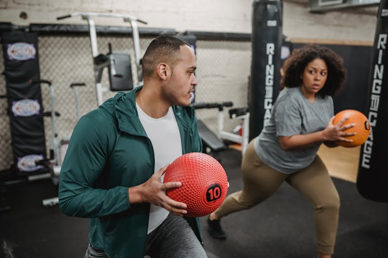 Focused African American overweight woman and professional instructor warming up together in modern gym