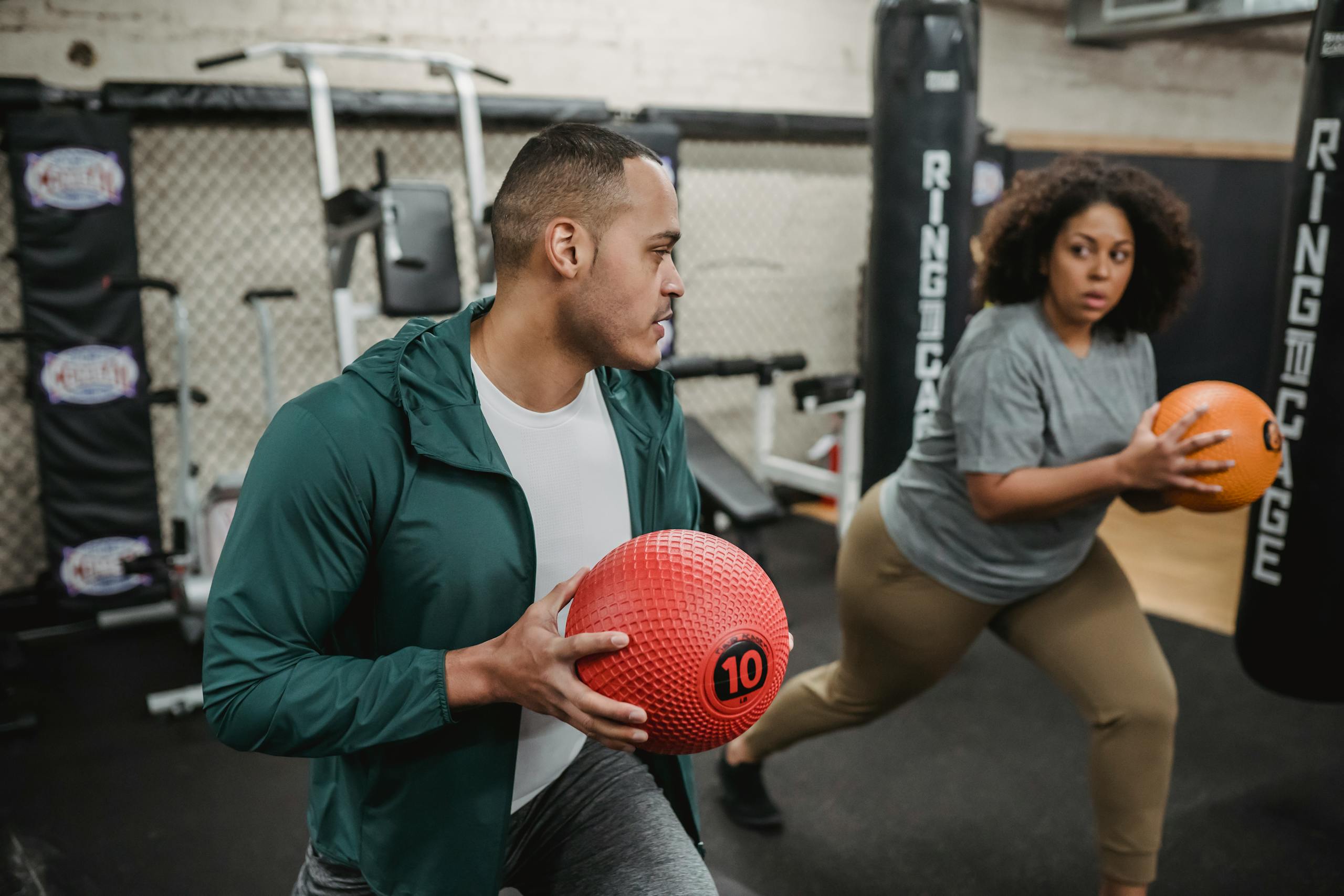 Focused African American overweight woman and professional instructor warming up together in modern gym